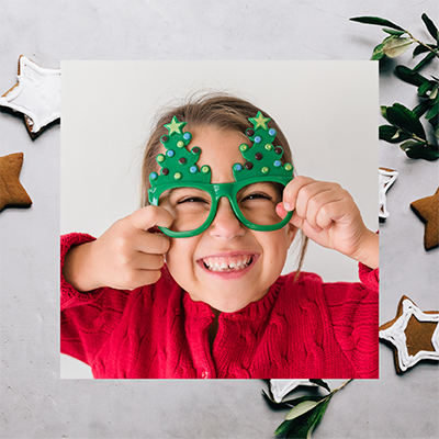 JLL_52538_F6b_Events_PNG_1mb_400sq_01kk Child holding Christmas tree-themed glasses frames, and star shaped cookies in the background